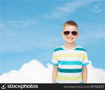 happiness, summer, childhood and people concept - smiling cute little boy in sunglasses over blue sky background