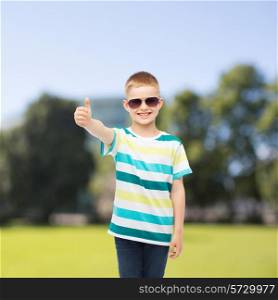 happiness, summer, childhood, gesture and people concept - smiling cute little boy in sunglasses over park background showing thumbs up