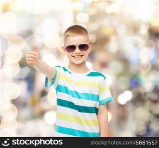 happiness, summer, gesture, childhood and people concept - smiling cute little boy in sunglasses over sparkling background showing thumbs up