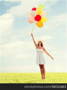happiness, summer, holidays and people concept - smiling young woman wearing sunglasses with balloons over blue sky and grass background