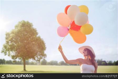 happiness, summer, holidays and people concept - smiling young woman wearing sunglasses with balloons over summer park background