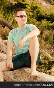 Happiness summer vacation and people concept. Fashion portrait handsome man on the beach, guy sitting on tree