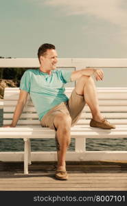 Happiness summer vacation and people concept. Fashion portrait of handsome man sitting in sun on bench sea landscape
