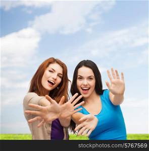 happiness, summer vacation, friendship and people concept - smiling teenage girls having fun over blue sky and grass background