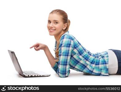 happiness, technology, internet and people concept - smiling young woman lying on floor with laptop computer and pointing finger