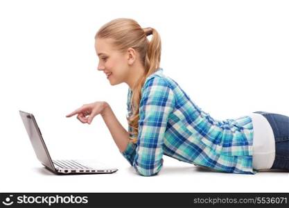 happiness, technology, internet and people concept - smiling young woman lying on floor with laptop computer and pointing finger