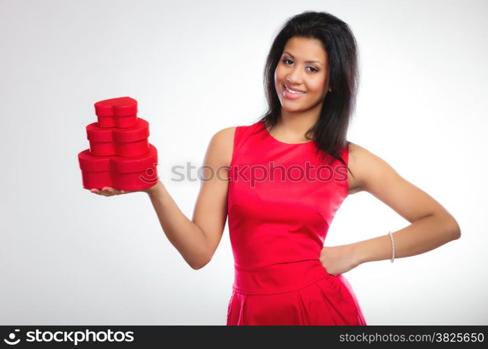 Happiness, valentines day and love concept. Attractive elegant smiling woman in red dress, girl mixed race holding red heart-shaped gift boxes on gray