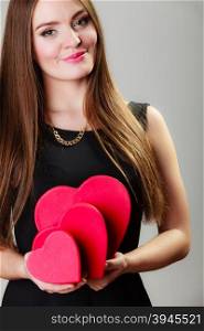 Happiness, valentines day and love concept. Lovely elegant woman in black dress with red heart-shaped gift boxes on gray