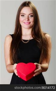 Happiness, valentines day and love concept. Lovely elegant woman in black dress with red heart-shaped gift box on gray