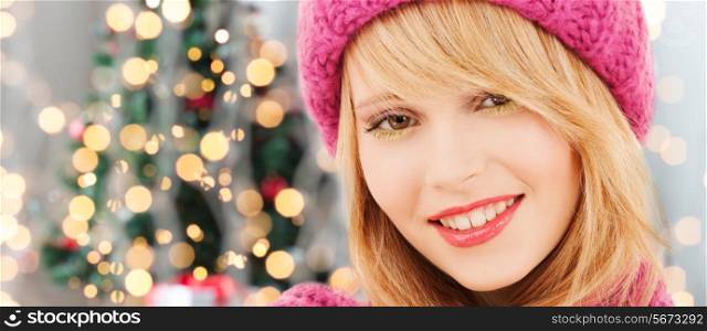 happiness, winter holidays and people concept - close up of smiling young woman in pink hat and scarf over christmas tree lights background