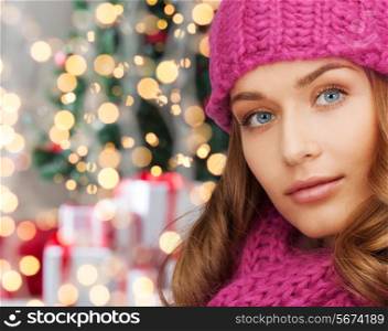 happiness, winter holidays and people concept - close up of smiling young woman in pink hat and scarf over christmas tree with presents background