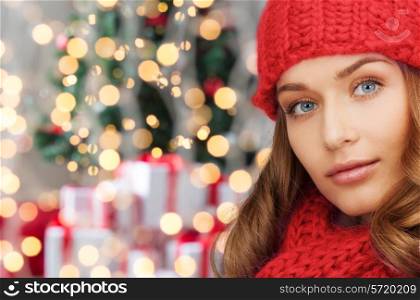 happiness, winter holidays and people concept - close up of smiling young woman in red hat and scarf over christmas tree lights background
