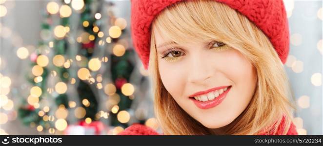 happiness, winter holidays and people concept - close up of smiling young woman in red hat and scarf over christmas tree lights background
