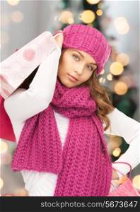 happiness, winter holidays and people concept - smiling young woman in hat and scarf with shopping bags over christmas tree background