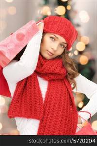 happiness, winter holidays and people concept - smiling young woman in hat and scarf with shopping bags over christmas tree background