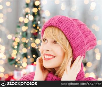 happiness, winter holidays and people concept - smiling young woman in pink hat and scarf over christmas tree lights background