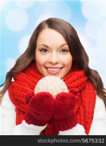 happiness, winter holidays and people concept - smiling young woman in red scarf and mittens with christmas ball over blue lights background