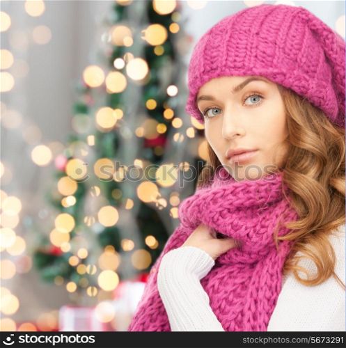 happiness, winter holidays and people concept - young woman in pink hat and scarf over christmas tree lights background