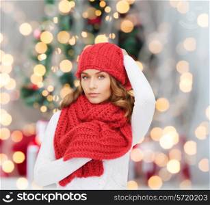 happiness, winter holidays and people concept - young woman in red hat and scarf over christmas tree lights background