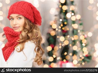 happiness, winter holidays and people concept - young woman in red hat and scarf over christmas tree lights background