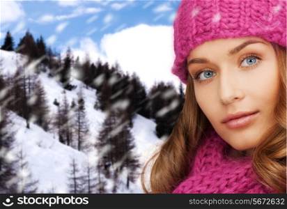 happiness, winter holidays, christmas and people concept - close up of smiling young woman in pink hat and scarf over snowy mountains background