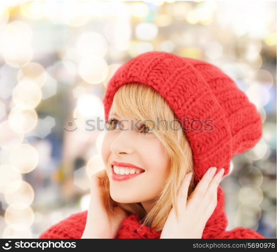 happiness, winter holidays, christmas and people concept - close up of smiling young woman in red hat and scarf over lights background