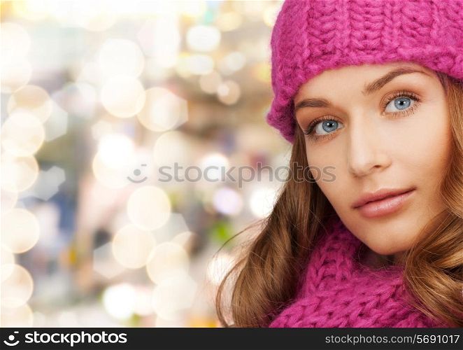 happiness, winter holidays, christmas and people concept - close up of smiling young woman in pink hat and scarf over lights background