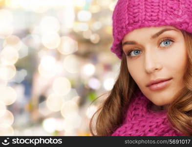 happiness, winter holidays, christmas and people concept - close up of smiling young woman in pink hat and scarf over lights background