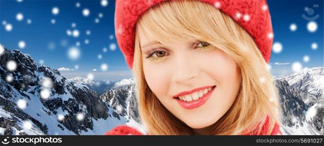 happiness, winter holidays, christmas and people concept - close up of smiling young woman in red hat and scarf over snowy mountains background