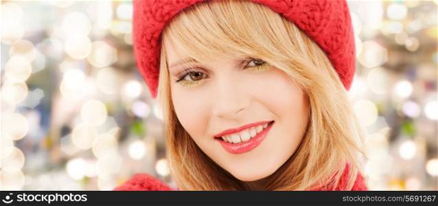 happiness, winter holidays, christmas and people concept - close up of smiling young woman in red hat and scarf over lights background