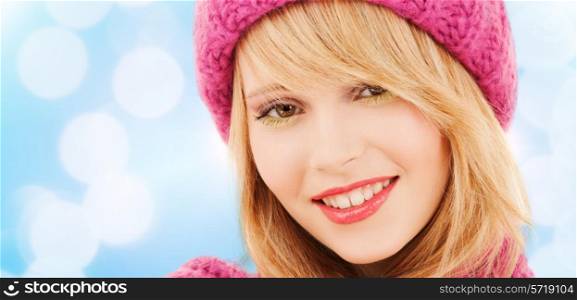 happiness, winter holidays, christmas and people concept - close up of smiling young woman in pink hat and scarf over blue lights background