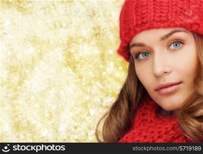 happiness, winter holidays, christmas and people concept - close up of smiling young woman in red hat and scarf over yellow lights background