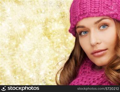 happiness, winter holidays, christmas and people concept - close up of smiling young woman in pink hat and scarf over yellow lights background