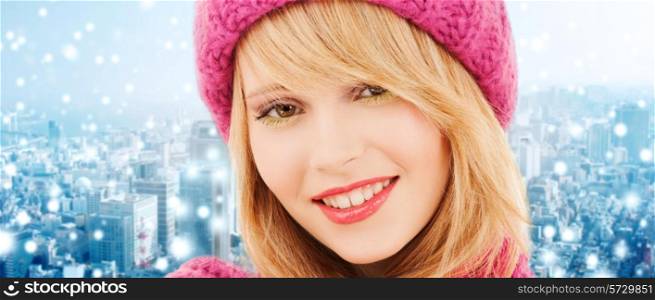 happiness, winter holidays, christmas and people concept - close up of smiling young woman in pink hat and scarf over blue snowy background