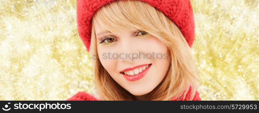 happiness, winter holidays, christmas and people concept - close up of smiling young woman in red hat and scarf over yellow lights background