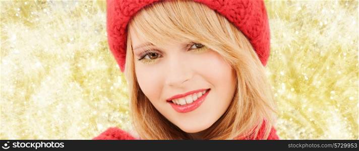 happiness, winter holidays, christmas and people concept - close up of smiling young woman in red hat and scarf over yellow lights background