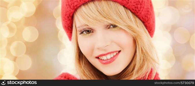 happiness, winter holidays, christmas and people concept - close up of smiling young woman in red hat and scarf over beige lights background