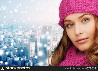 happiness, winter holidays, christmas and people concept - close up of smiling young woman in pink hat and scarf over snowy city background