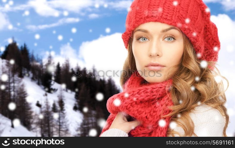 happiness, winter holidays, christmas and people concept - close up of young woman in red hat and scarf over snowy mountains background