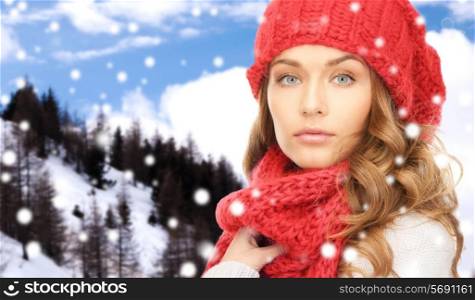 happiness, winter holidays, christmas and people concept - close up of young woman in red hat and scarf over snowy mountains background
