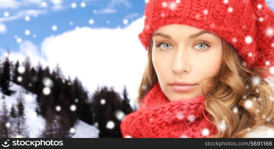 happiness, winter holidays, christmas and people concept - close up of young woman in red hat and scarf over snowy mountains background