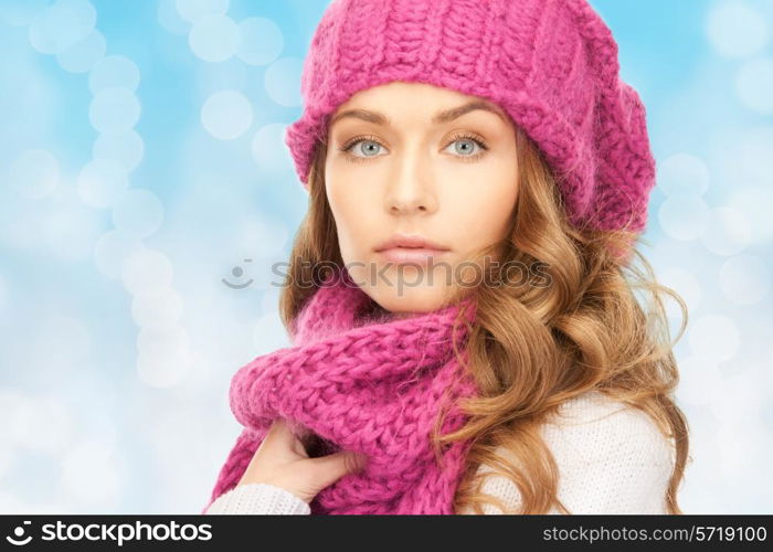 happiness, winter holidays, christmas and people concept - close up of young woman in pink hat and scarf over blue lights background