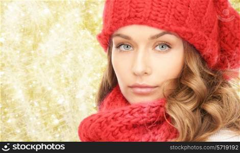 happiness, winter holidays, christmas and people concept - close up of young woman in red hat and scarf over yellow lights background