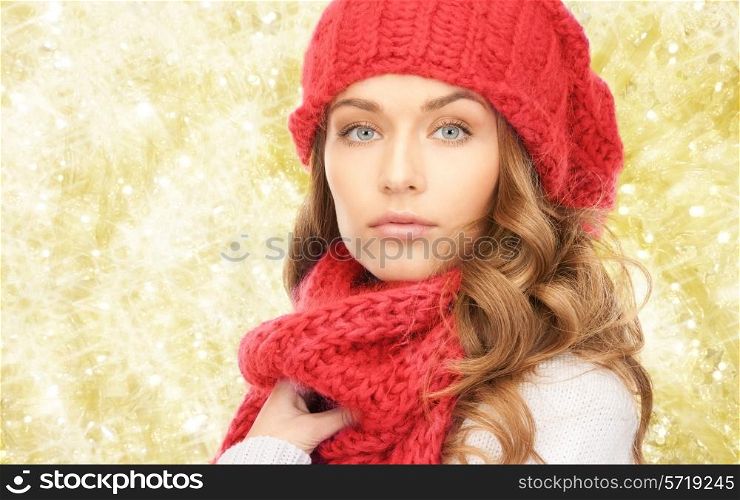 happiness, winter holidays, christmas and people concept - close up of young woman in red hat and scarf over yellow lights background