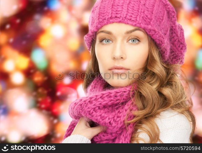 happiness, winter holidays, christmas and people concept - close up of young woman in pink hat and scarf over red lights background