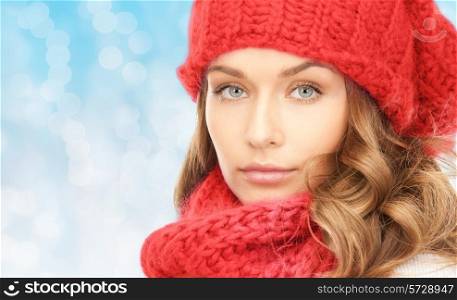 happiness, winter holidays, christmas and people concept - close up of young woman in red hat and scarf over blue lights background