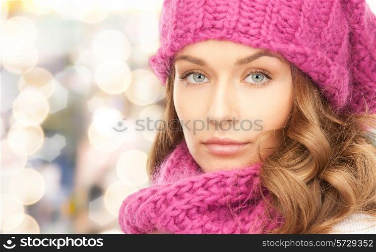 happiness, winter holidays, christmas and people concept - close up of young woman in pink hat and scarf over lights background