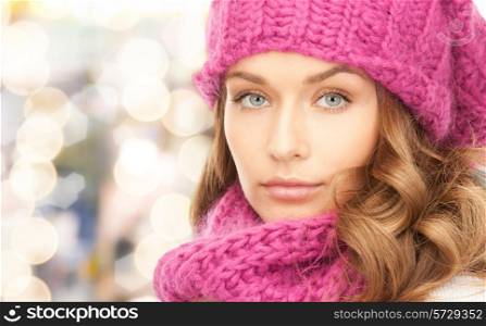 happiness, winter holidays, christmas and people concept - close up of young woman in pink hat and scarf over lights background
