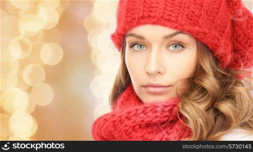 happiness, winter holidays, christmas and people concept - close up of young woman in red hat and scarf over beige lights background