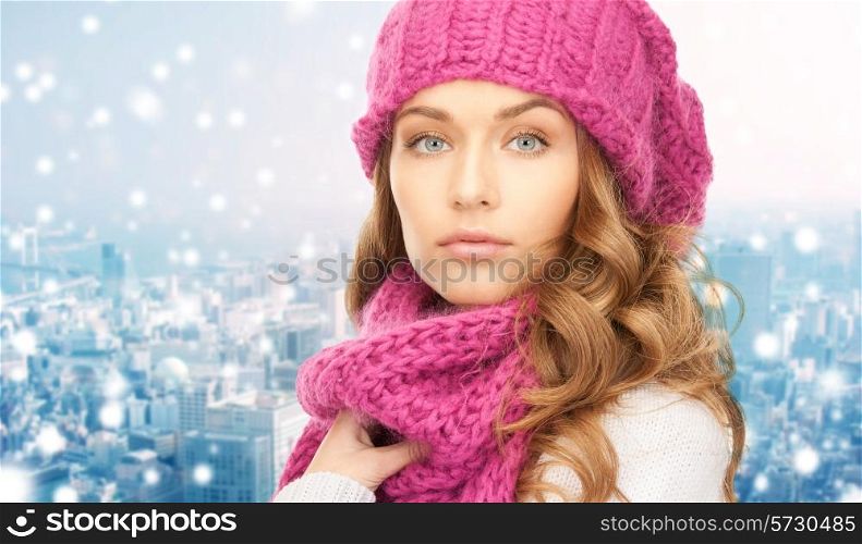 happiness, winter holidays, christmas and people concept - close up of young woman in pink hat and scarf over blue snowy background